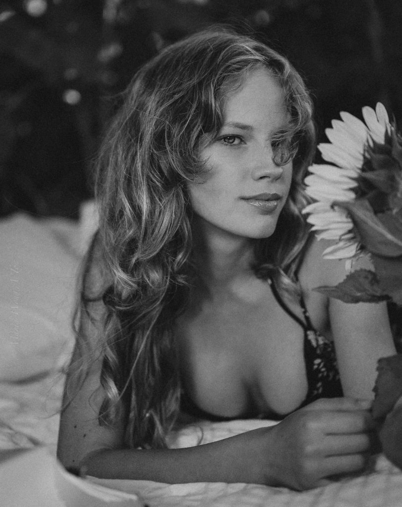 Over-the-shoulder view of a woman in a floral dress holding a sunflower, with a vintage typewriter in the foreground, all set against a moody, dark backdrop, evoking a nostalgic and creative atmosphere