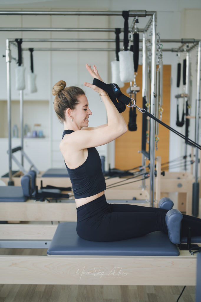 A woman dressed in a black Pilates outfit performing an exercise on a Pilates reformer.