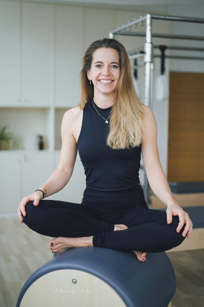 A woman dressed in a black Pilates outfit performing an exercise on a Pilates reformer
